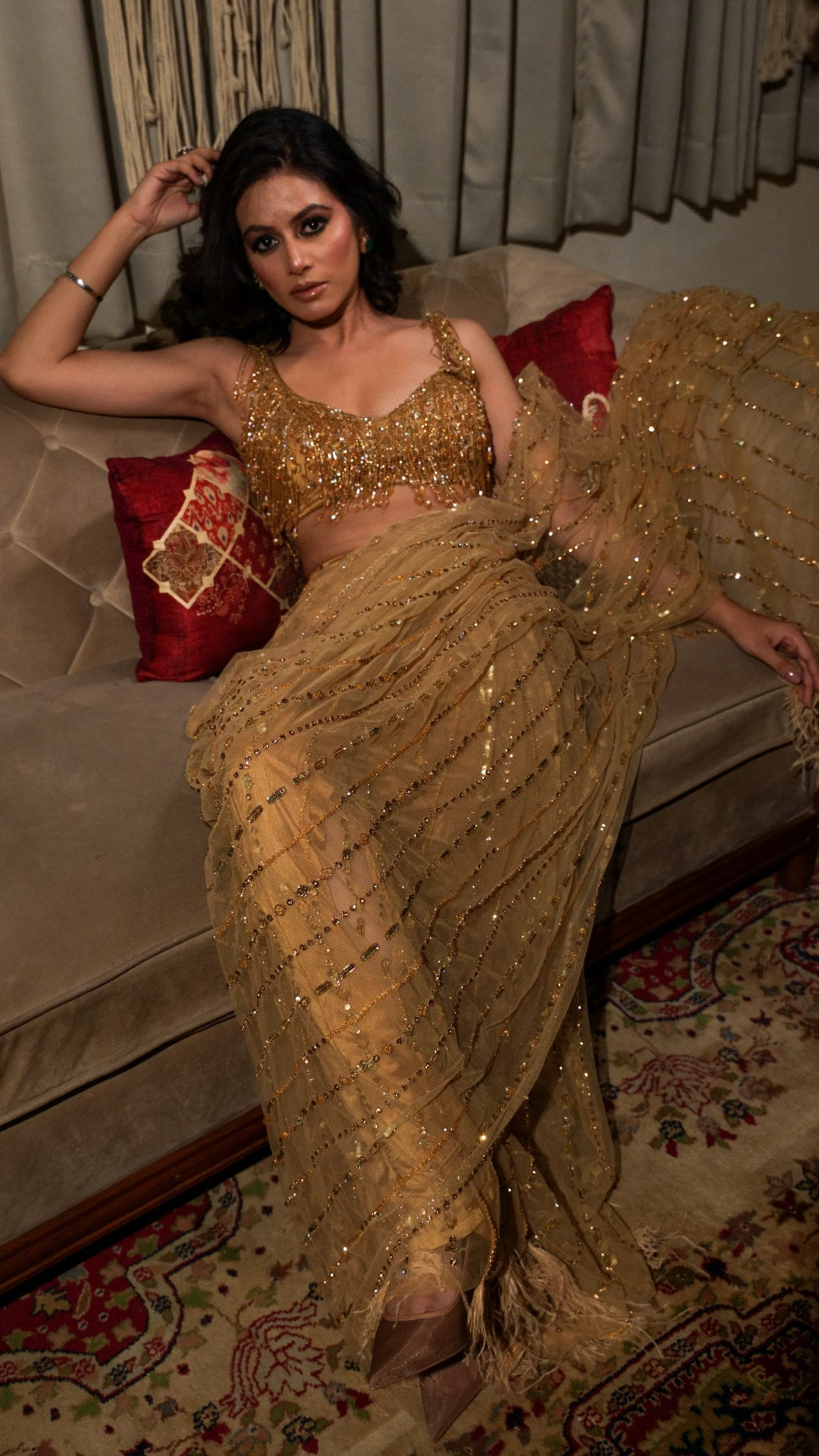 Woman in a gold saree sitting on a couch with decorative pillows.