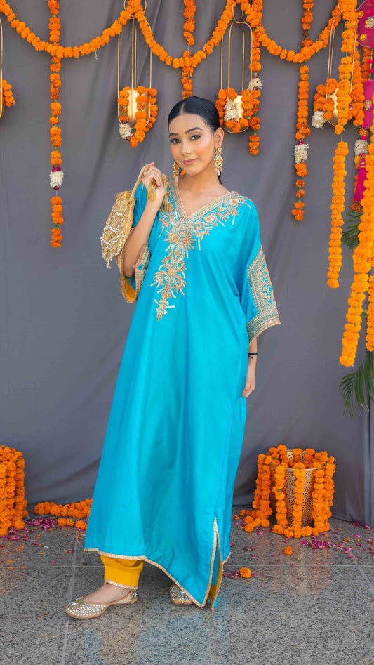Woman in a blue traditional outfit with gold embroidery standing in front of floral decorations.