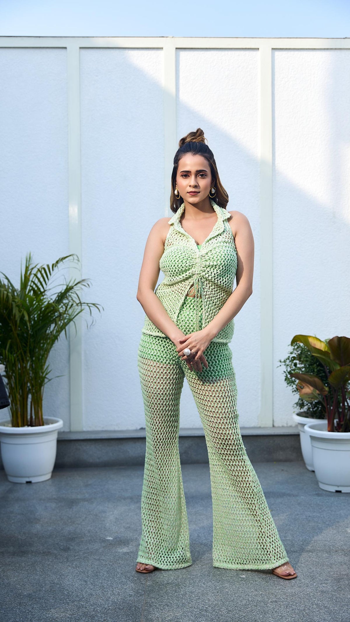 Woman in a green outfit standing on a rooftop with plants in the background