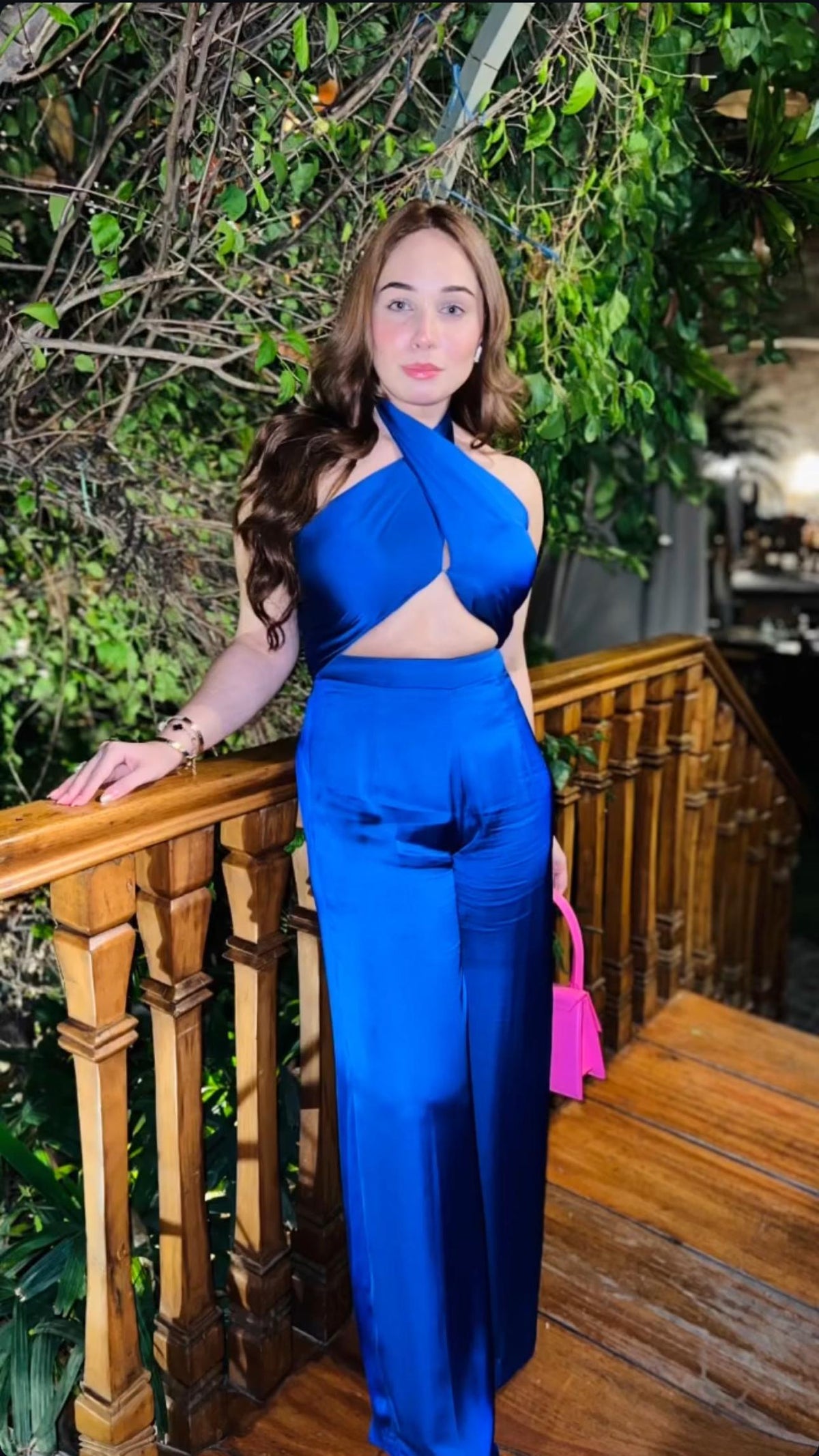 Woman in a blue outfit standing on a wooden staircase with greenery in the background