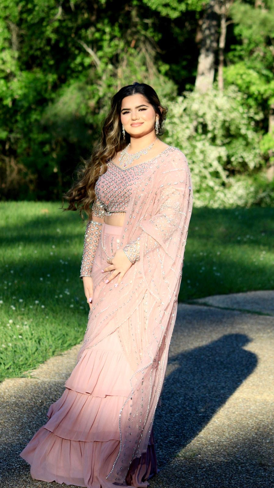 Woman in a pink saree standing outdoors with greenery in the background