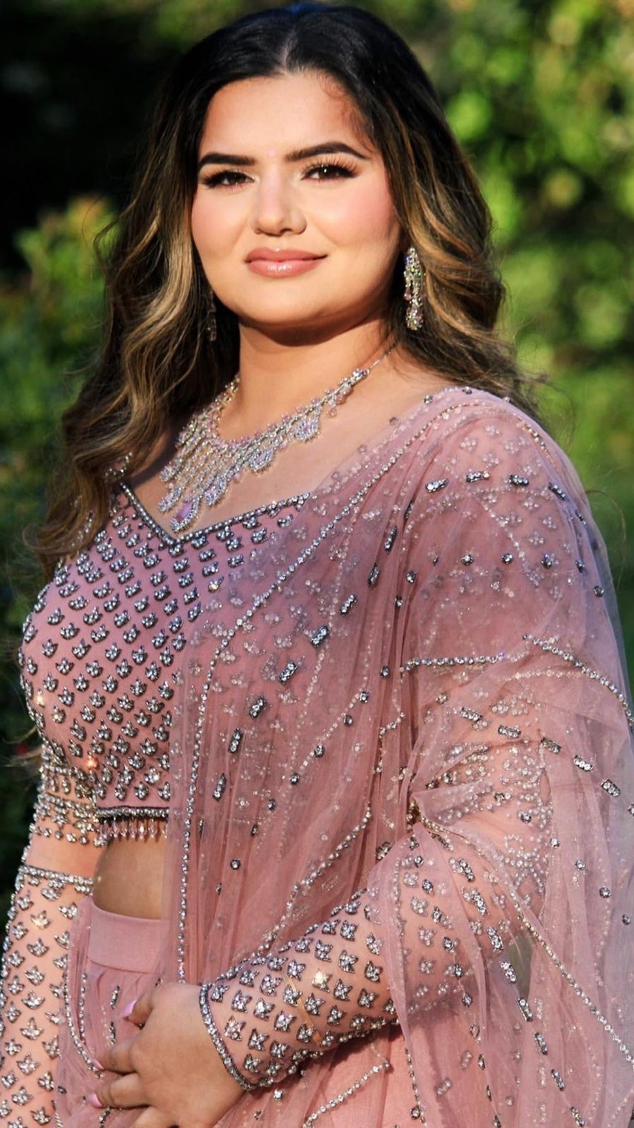 Woman wearing a pink saree with intricate designs against a blurred green background