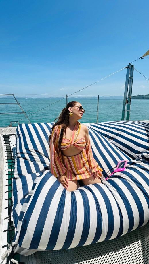Woman in a striped swimsuit sitting on a blue and white striped lounge chair by the sea.