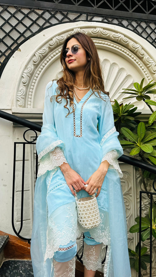Woman in light blue outfit standing in front of decorative archway with plants.