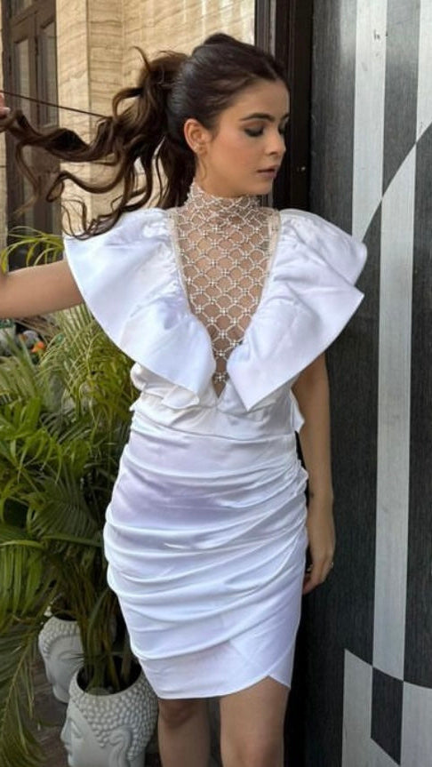 Woman in a white dress standing next to a decorative wall with plants in the background
