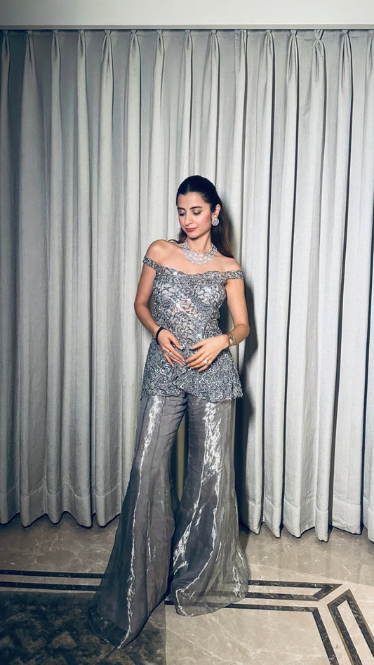 Woman in a silver off-shoulder outfit standing in front of a curtain.