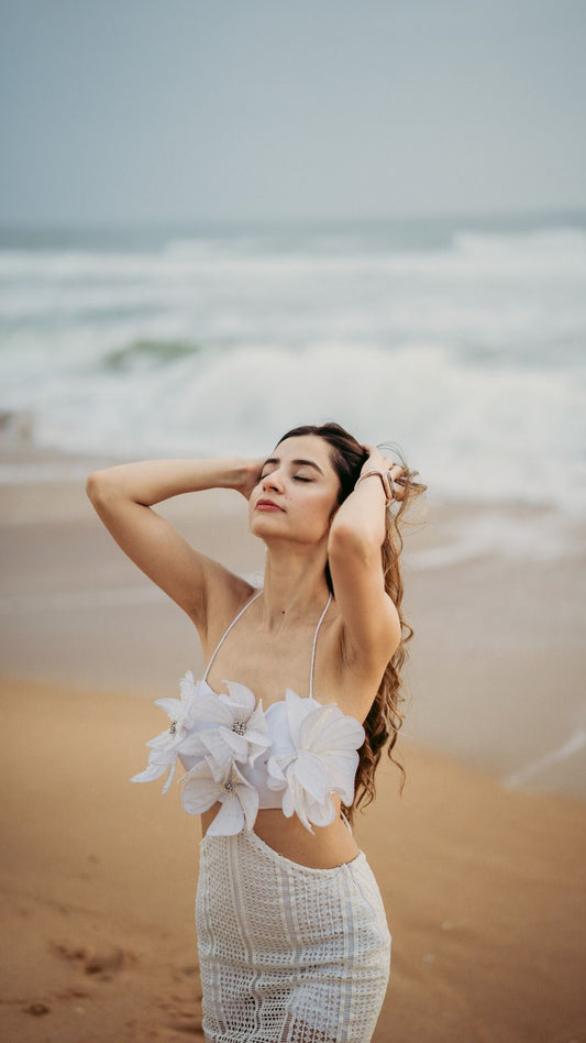 Woman in a white outfit standing on a beach with ocean waves in the background