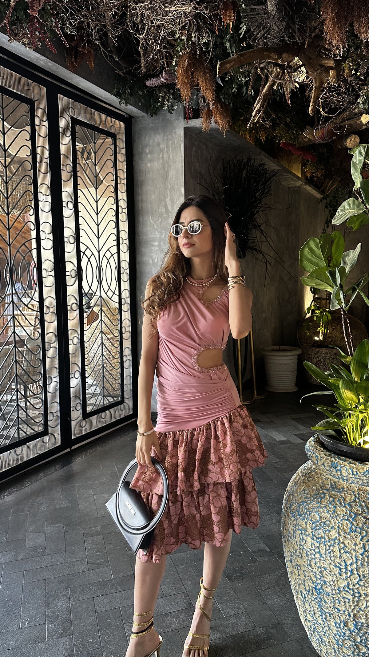 Woman in a pink dress standing in an indoor setting with plants and decorative elements.