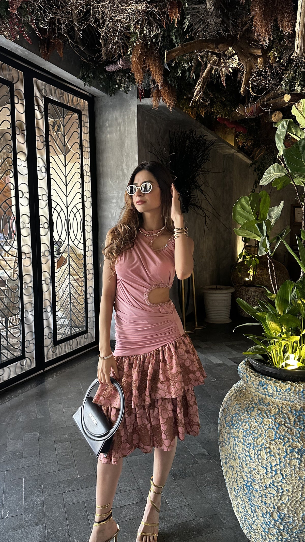 Woman in a pink dress standing in an indoor setting with plants and decorative elements.